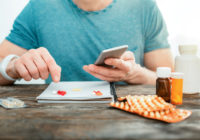 Concentrated attentive man pointing at pills holding the cellphone