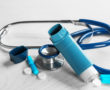 Asthma inhaler, stethoscope and pills on white wooden background