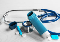Asthma inhaler, stethoscope and pills on white wooden background