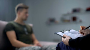 Psicólogo tomando notas durante la sesión de terapia con soldado masculino