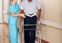 Nurse helping patient walk down hospital corridor