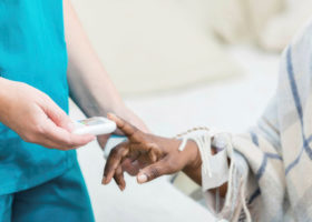 An image of a nurse testing the blood sugar of a patient using a handheld device.