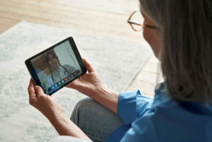 A patient wearing glasses holds an electronic tablet on which there is a video call with a nurse