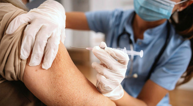 A patient receiving a vaccine injection into the upper arm from a medical professional