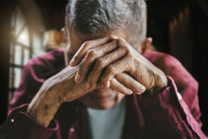 An older person covering their face with their hands 