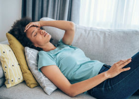Sick young woman lying on the couch and holding her head with her hand.