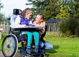 Child in wheelchair outside with a care assistant