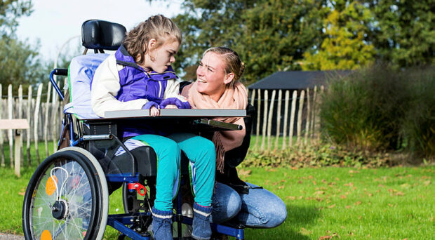 Child in wheelchair outside with a care assistant
